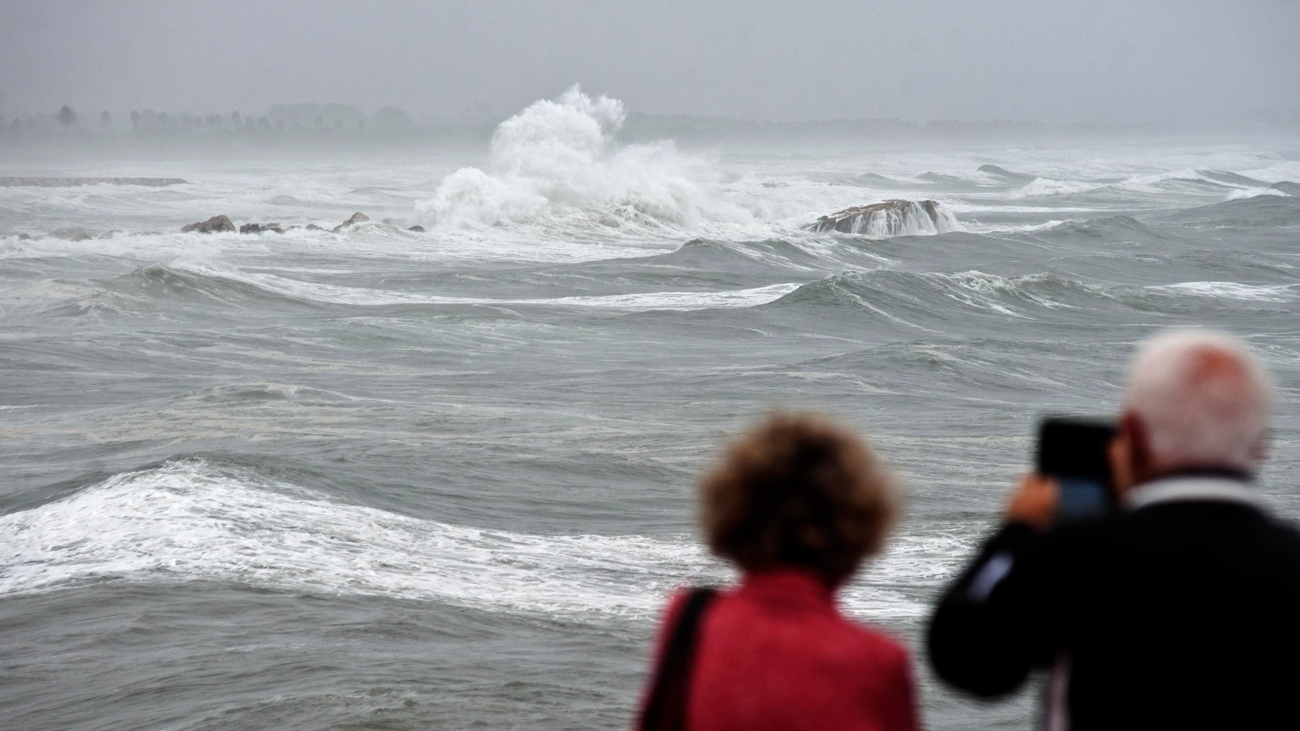 Unos vecinos toman imágenes en una playa afectada por un fuerte temporal