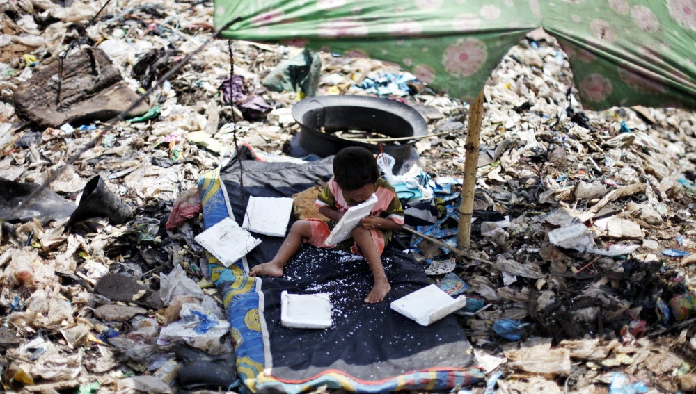 Un niño espera a que sus padres terminen de recoger material reciclable en un basurero de Indonesia