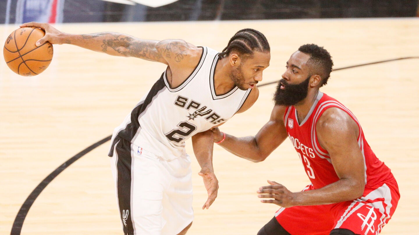 Kawhi Leonard sostiene el bal&oacute;n con una mano ante la defensa de James Harden