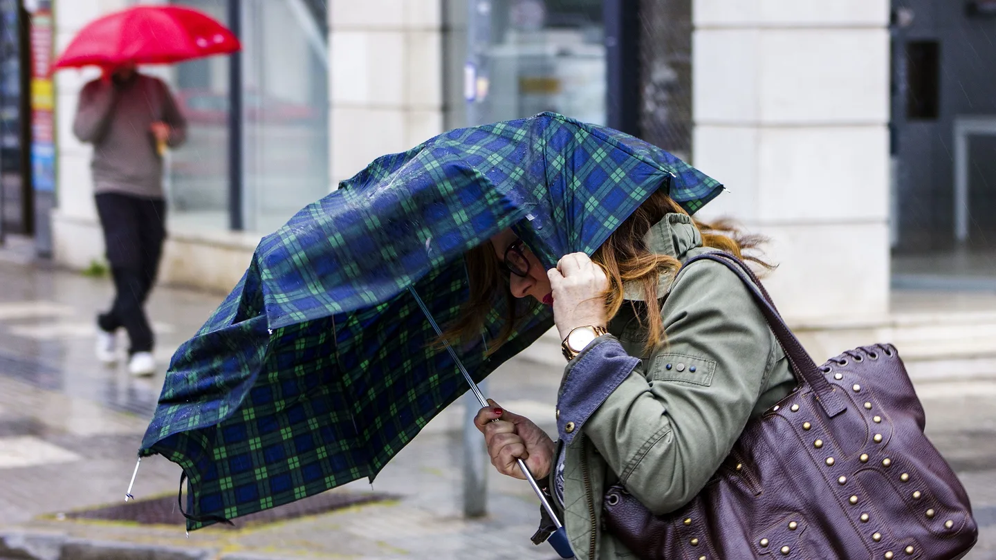 Una mujer intenta sujetar el paraguas que le protege de la lluvia debido al fuerte viento Una mujer intenta sujetar el paraguas que le protege de la lluvia debido al fuerte viento