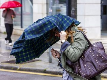 Una mujer intenta sujetar el paraguas que le protege de la lluvia debido al fuerte viento Una mujer intenta sujetar el paraguas que le protege de la lluvia debido al fuerte viento