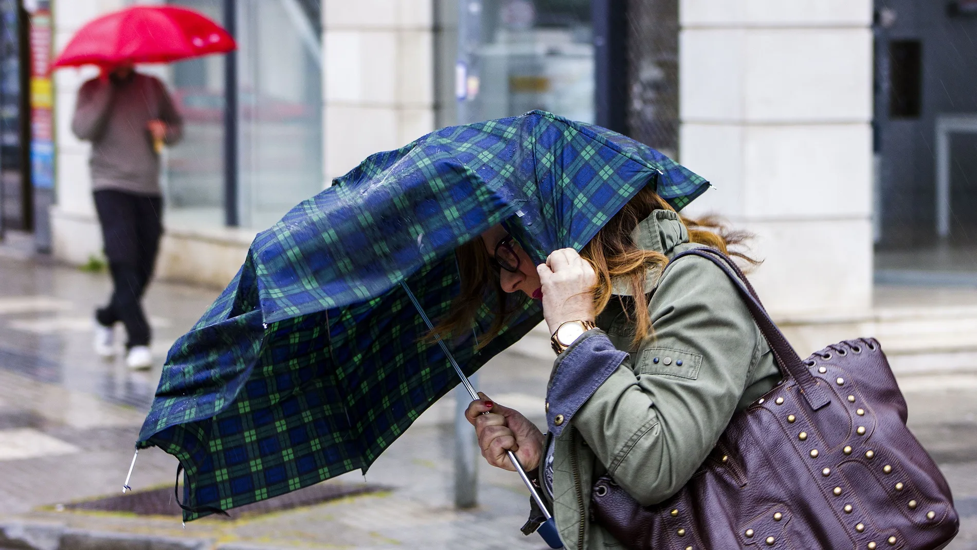 Una mujer intenta sujetar el paraguas que le protege de la lluvia debido al fuerte viento