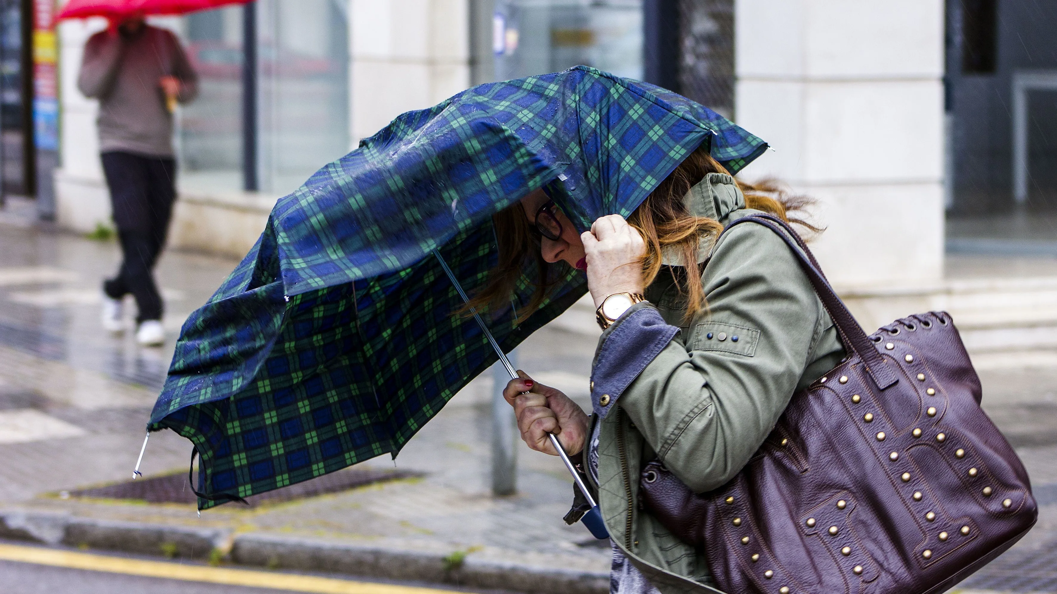 Una mujer intenta sujetar el paraguas que le protege de la lluvia debido al fuerte viento