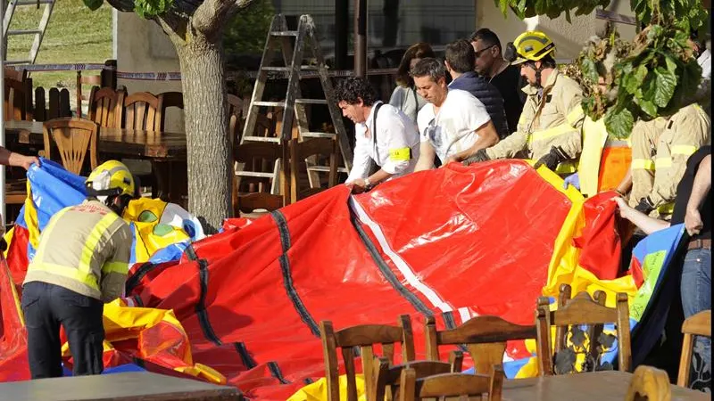 Varios operarios y bomberos retiran el castillo hinchable del restaurante Mas Oller