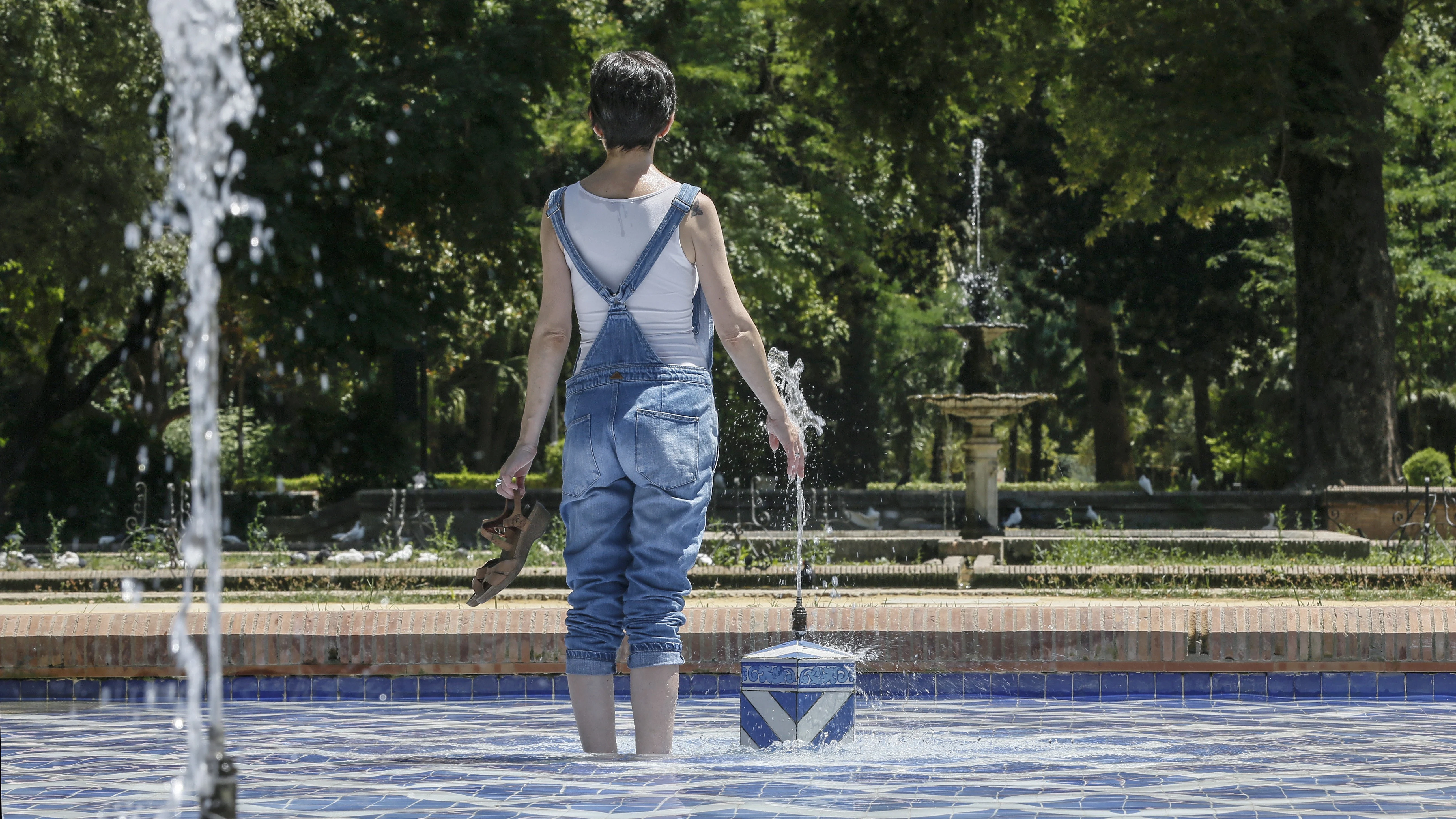 Una chica se refresca del intenso calor en una fuente del parque de Maria Luisa de Sevilla