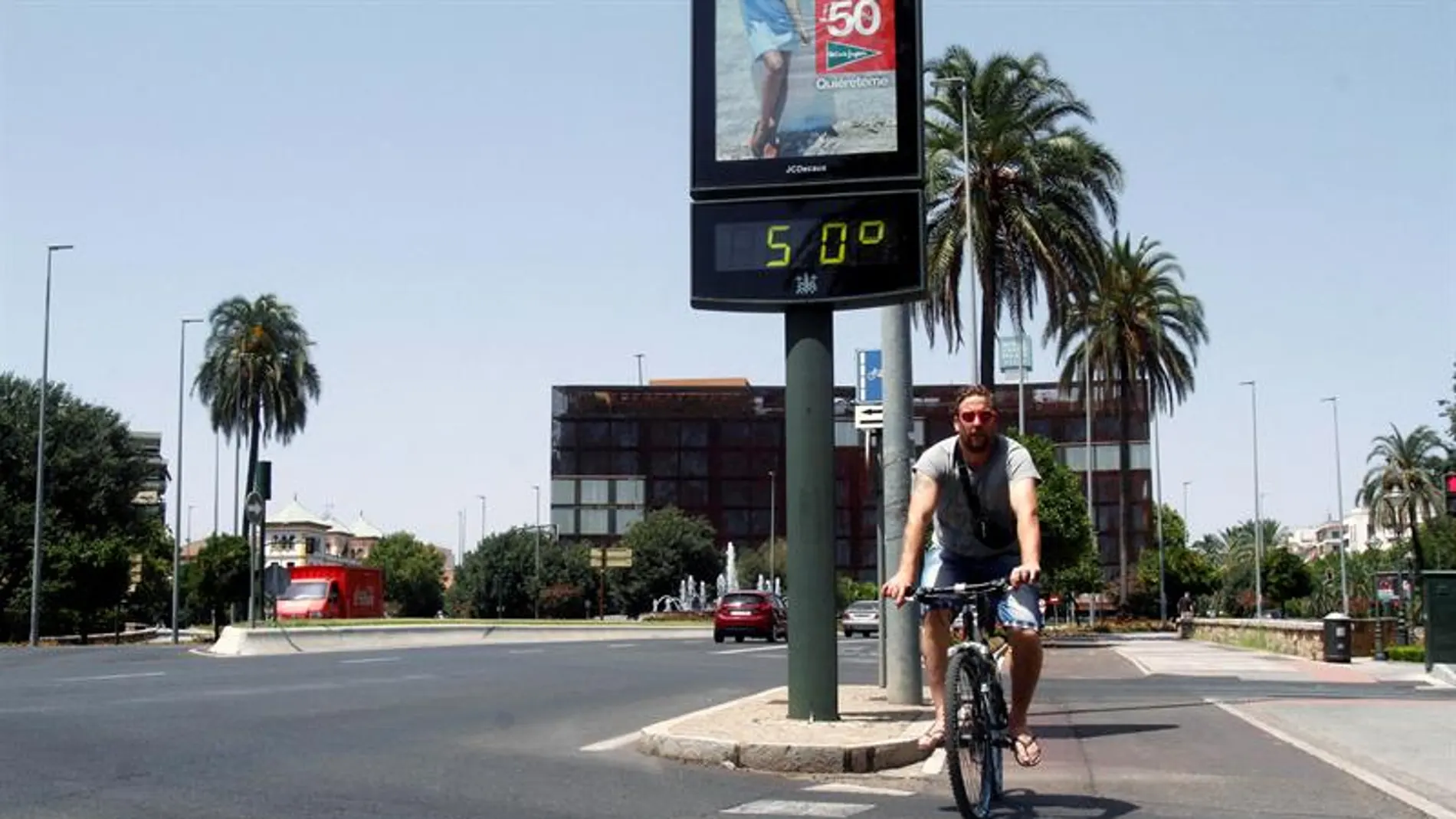 Un joven pasa con su bicicleta junto a un termómetro que marca 50 grados en una calle de Córdoba