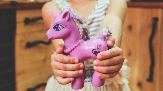 Una niña sostiene con sus manos un unicornio de juguete Una niña sostiene con sus manos un unicornio de juguete