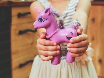 Una niña sostiene con sus manos un unicornio de juguete Una niña sostiene con sus manos un unicornio de juguete
