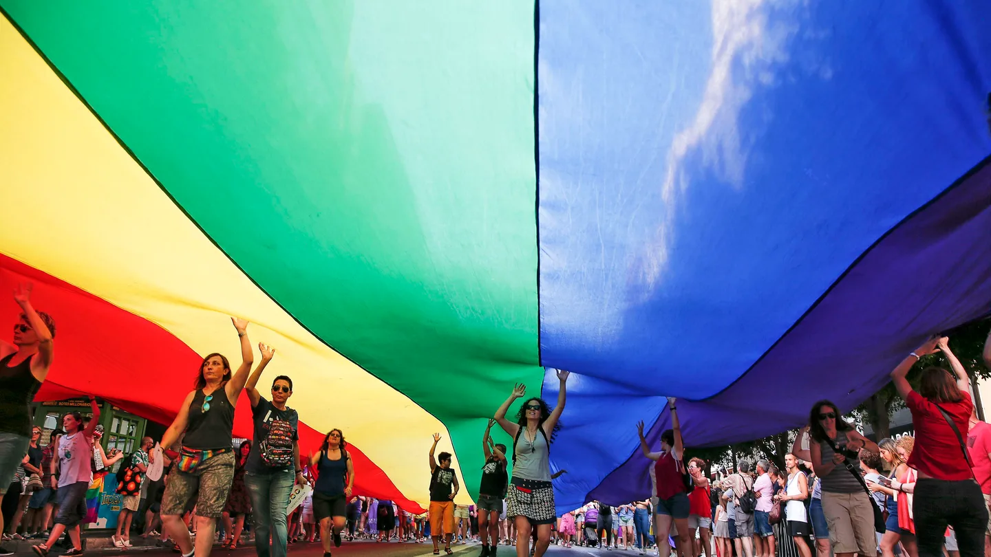 Varias personas portan una bandera arcoriris gigante Varias personas portan una bandera arcoriris gigante