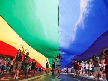 Varias personas portan una bandera arcoriris gigante Varias personas portan una bandera arcoriris gigante