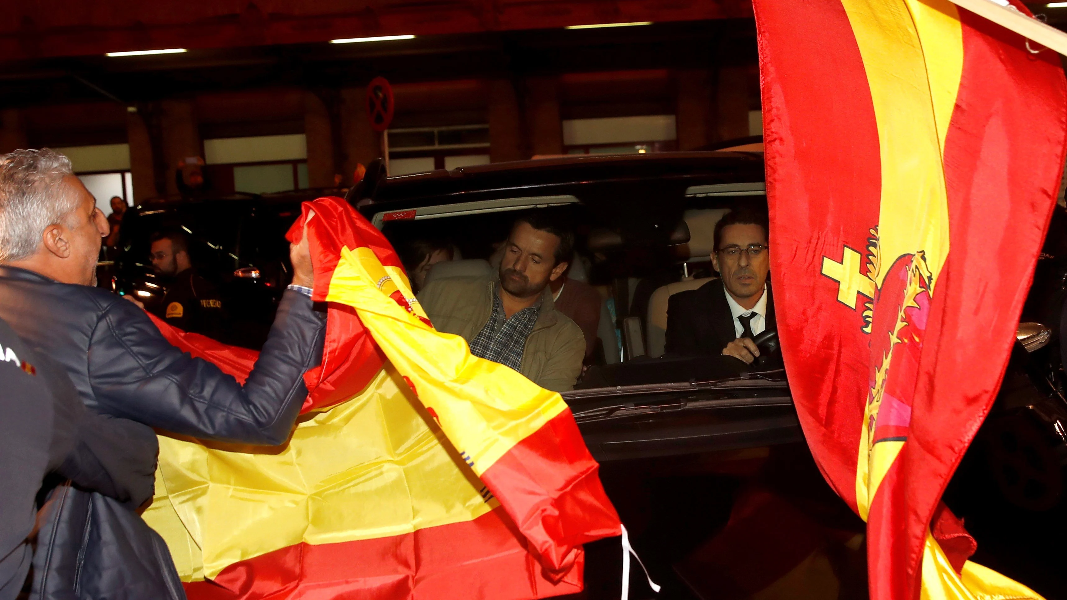 Un grupo de personas con banderas españolas rodean el coche de los miembros de la mesa del Parlament