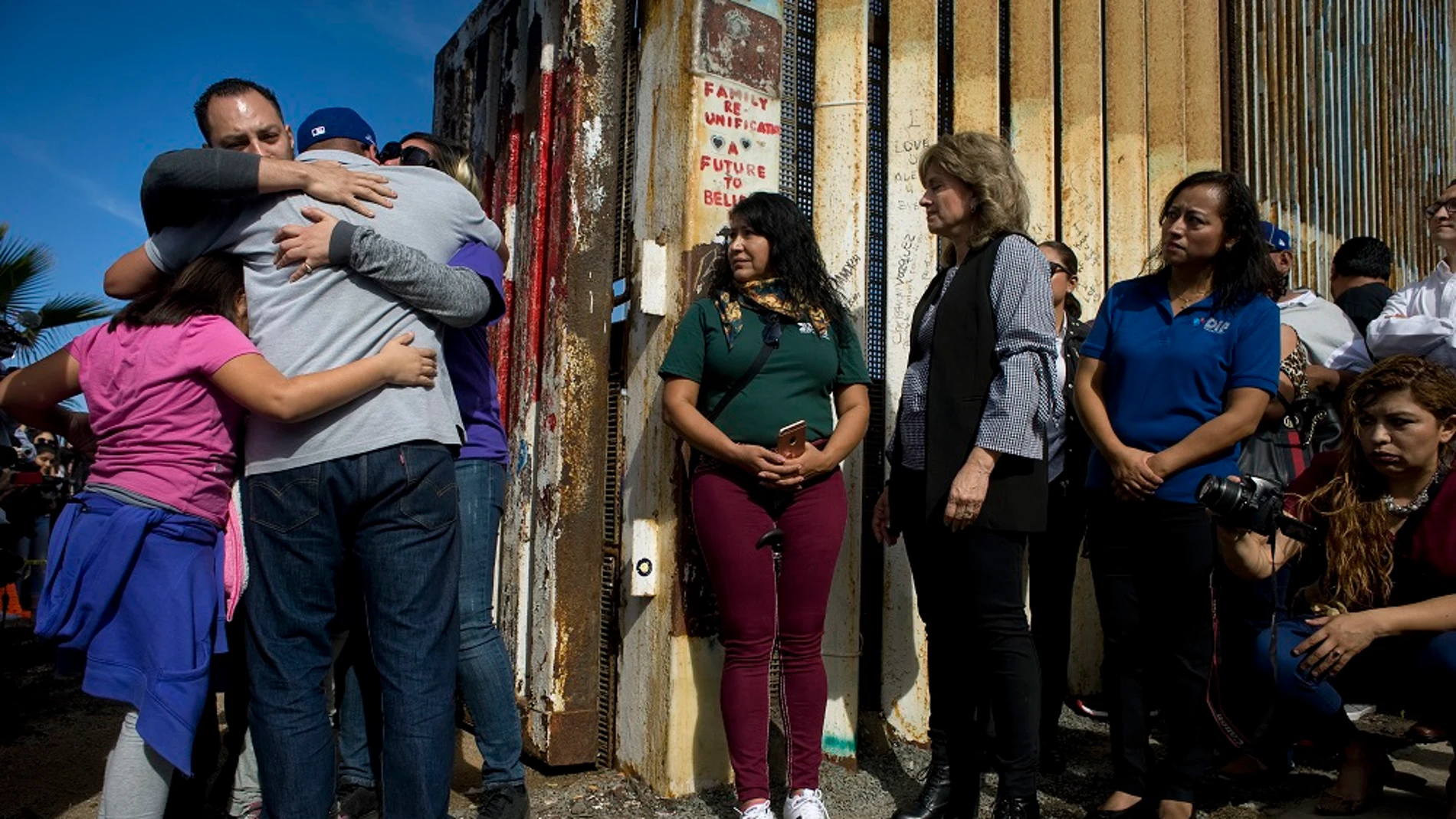 Un grupo de personas abrazan a sus familiares en una de las puertas de la valla fronteriza entre Estados Unidos y México 