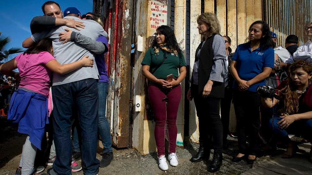 Un grupo de personas abrazan a sus familiares en una de las puertas de la valla fronteriza entre Estados Unidos y México 