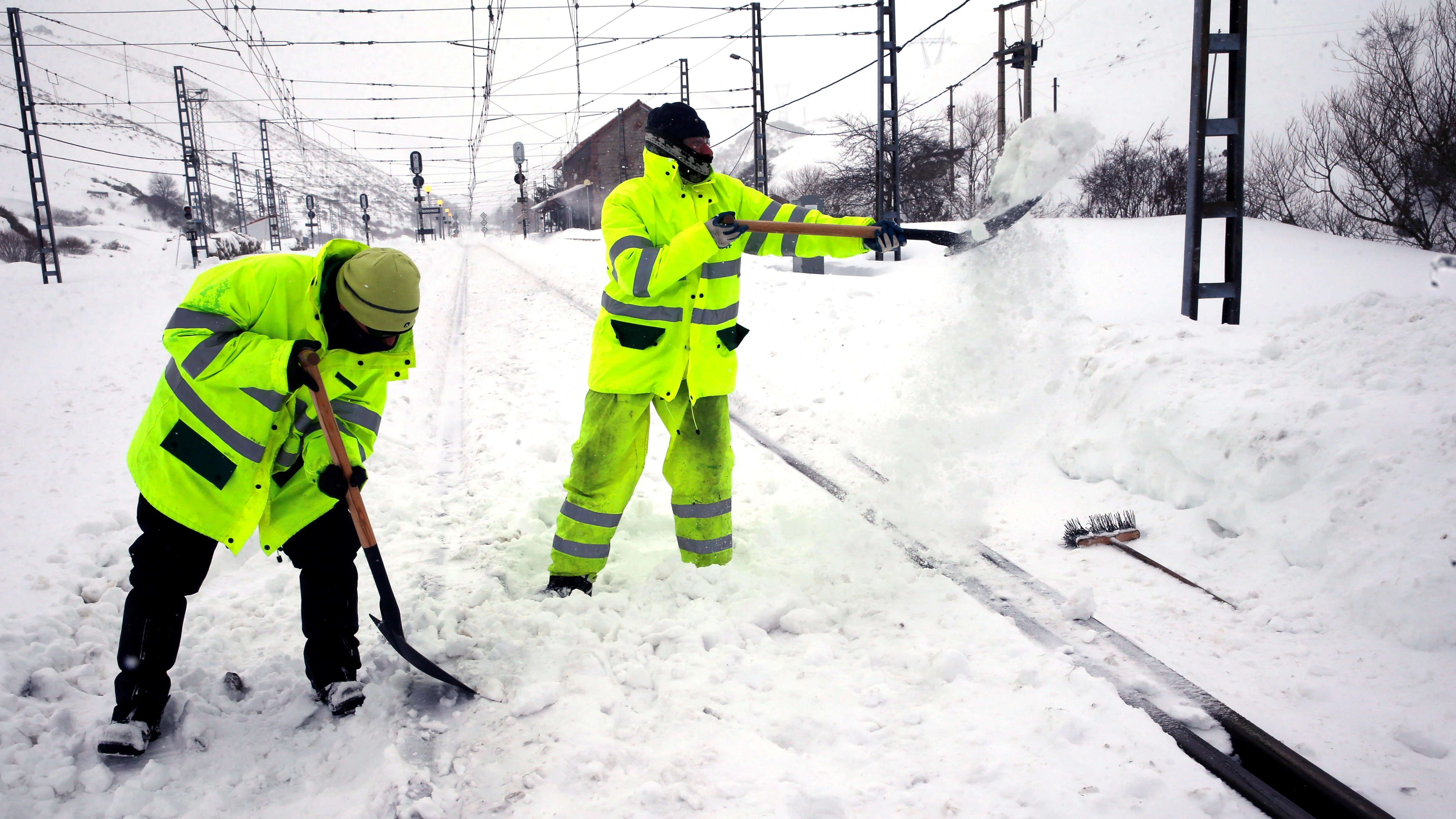 Dos operarios retiran la nieve en la estación de ferrocarril de Busdongo