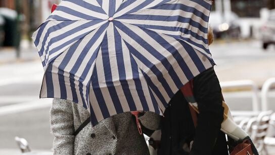 Dos mujeres se protegen con un parag&uuml;as de la lluvia y el viento 