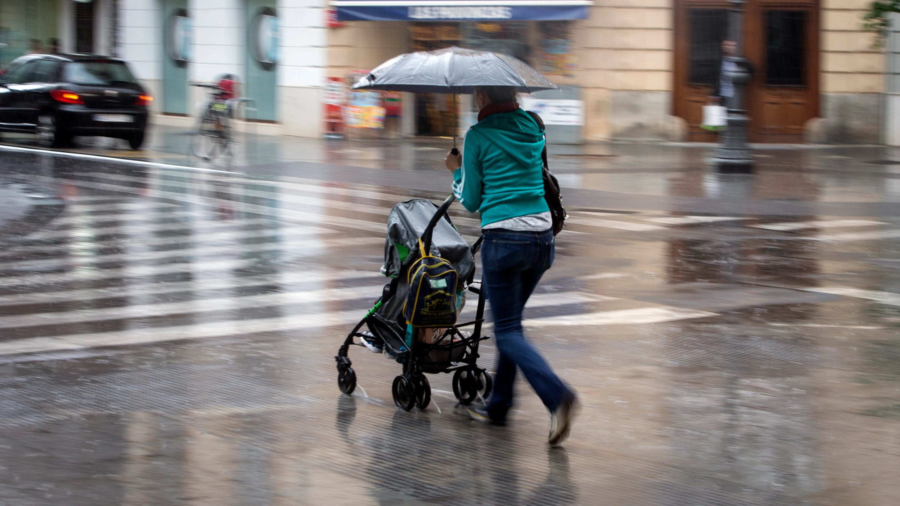 Una mujer con un carrito se protege con un paraguas de la lluvia