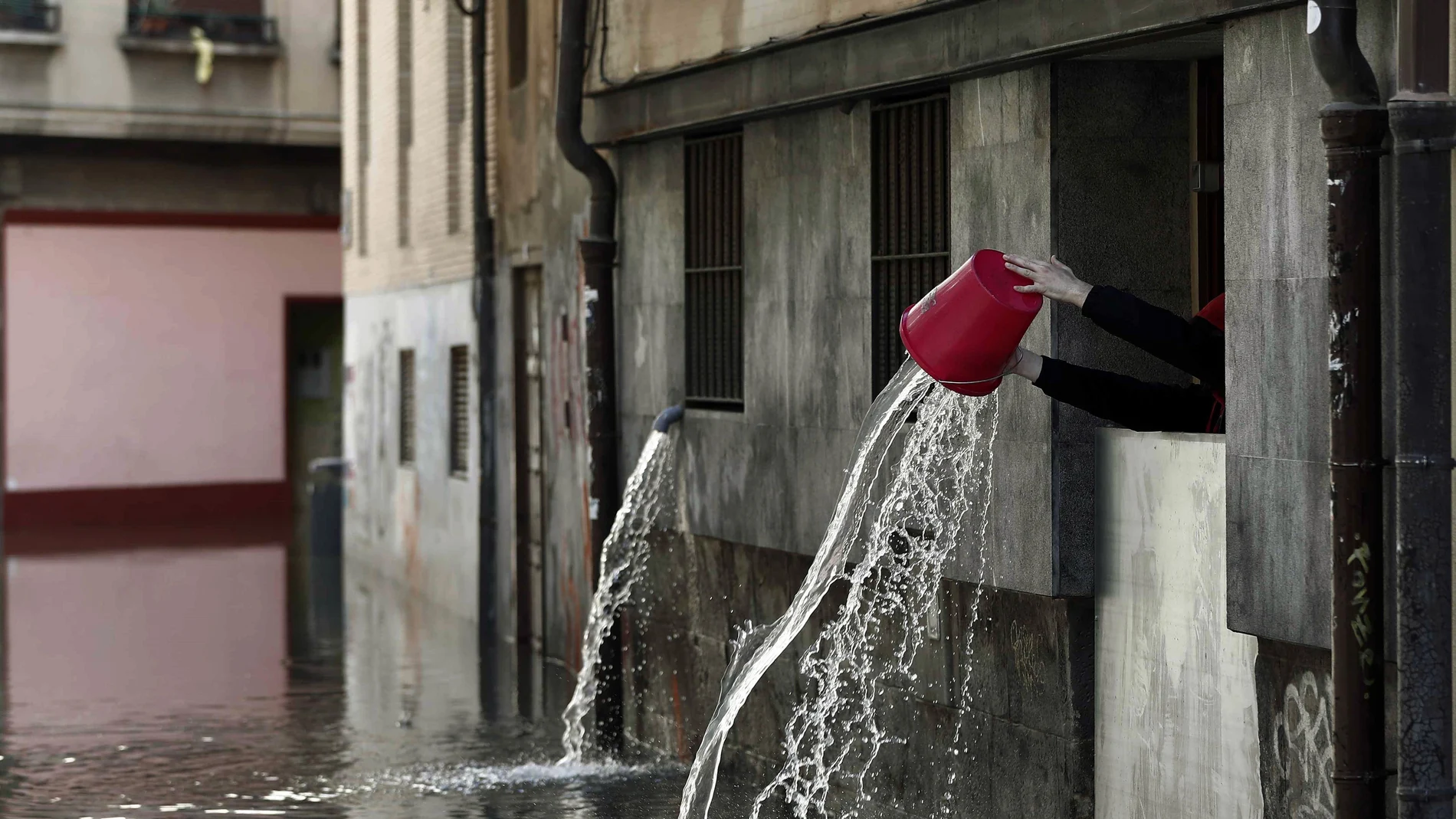 Una persona vierte el agua recogida que ha entrado en las cocinas de un restaurante de Tudela