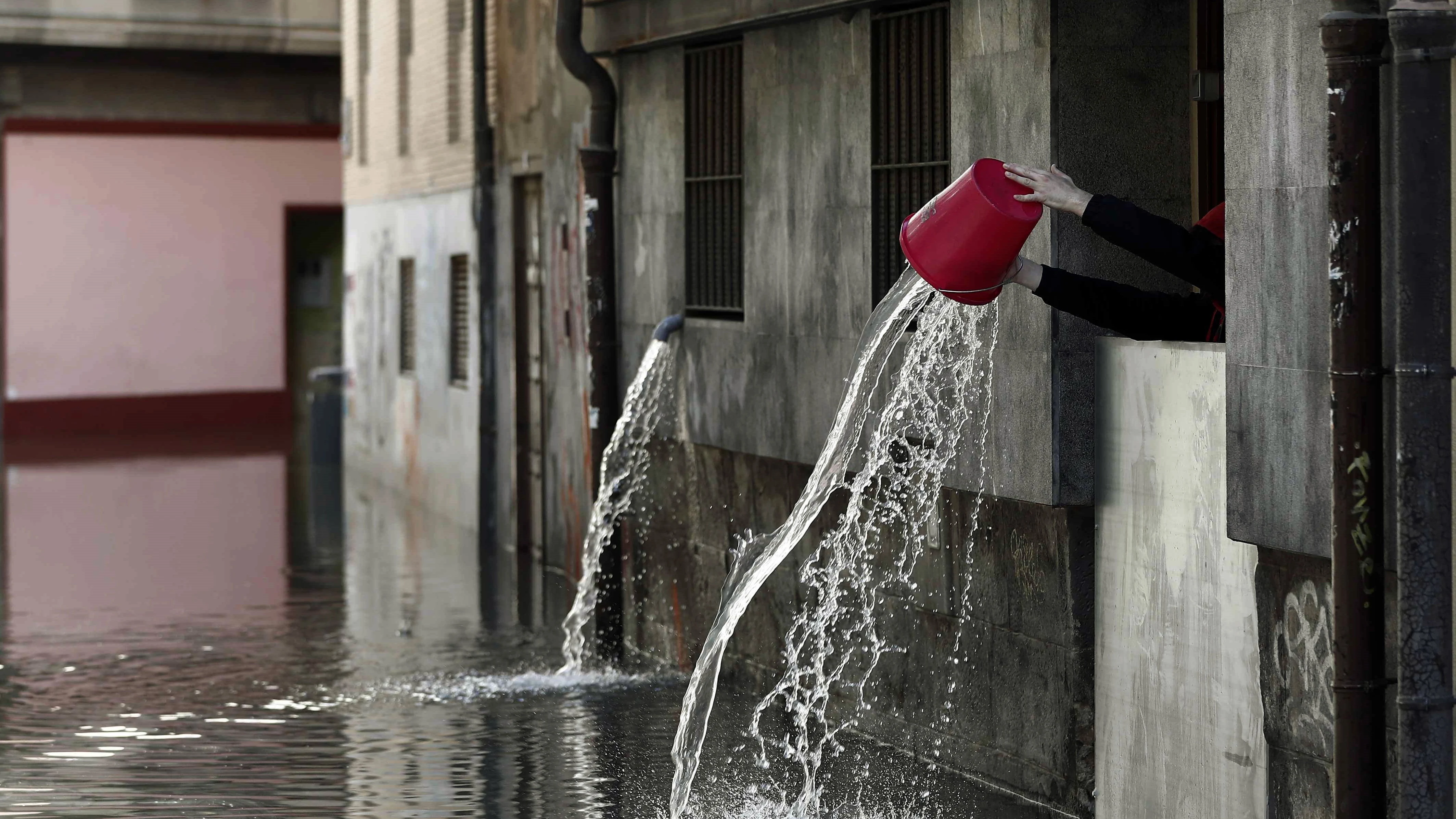 Una persona vierte el agua recogida que ha entrado en las cocinas de un restaurante de Tudela