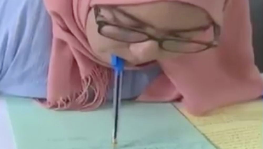 Una joven con parálisis en brazos y piernas escribe un examen con el bolígrafo en la boca