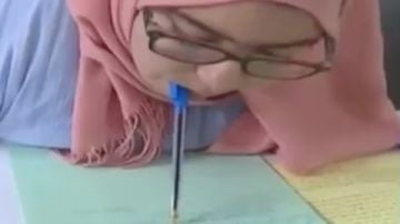 Una joven con parálisis en brazos y piernas escribe un examen con el bolígrafo en la boca