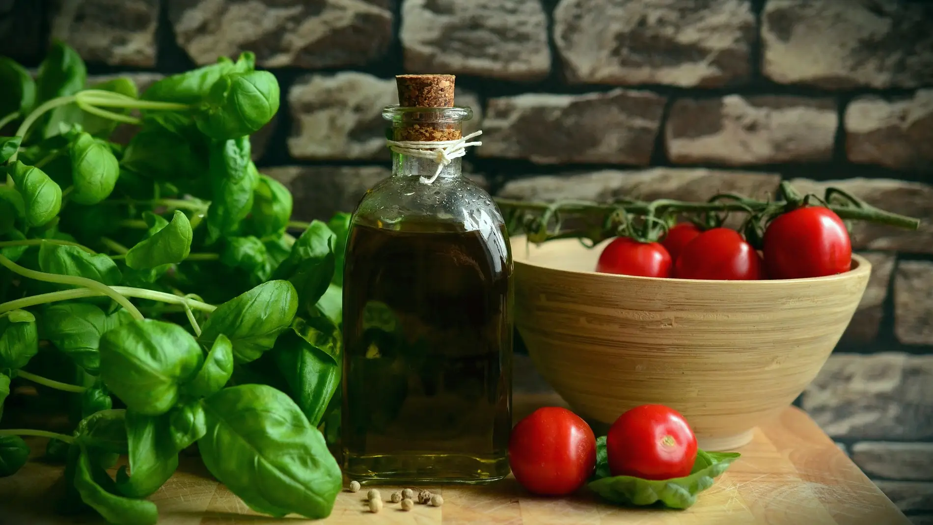 Productos típicos de la dieta mediterránea sobre una mesa de madera: una botella de aceite, un cuenco con tomates y hojas de albahaca
