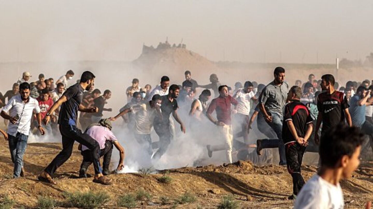 Decenas de palestinos se ponen a cubierto del gas lacrim&oacute;eno lanzado por soldados israel&iacute;es durante protestas en la frontera de Gaza con Israel