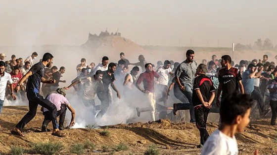 Decenas de palestinos se ponen a cubierto del gas lacrimóeno lanzado por soldados israelíes durante protestas en la frontera de Gaza con Israel