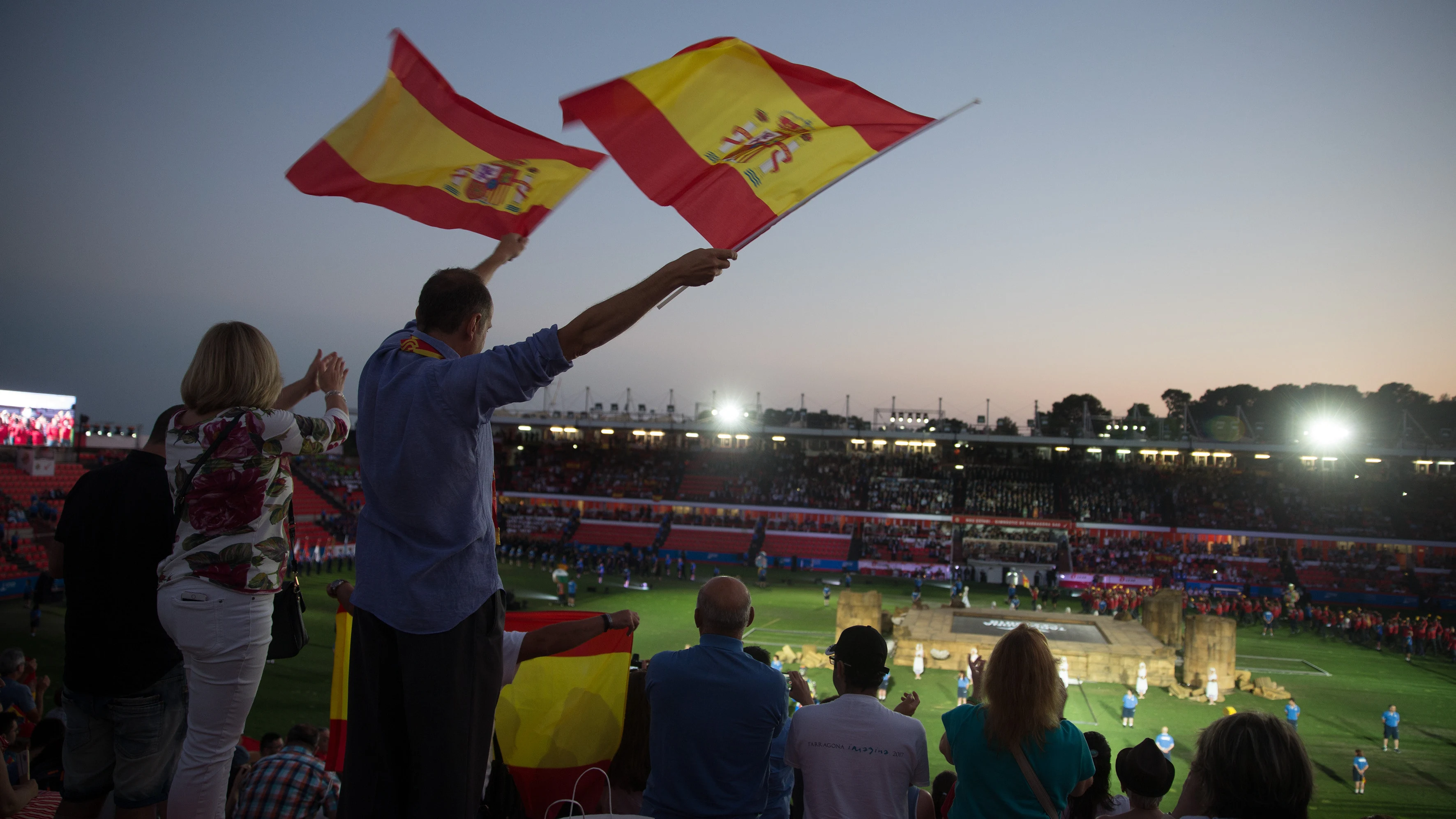 Dos personas agitan banderas al paso de los atletas españoles durante la inauguración de los XVIII Juegos Mediterráneos