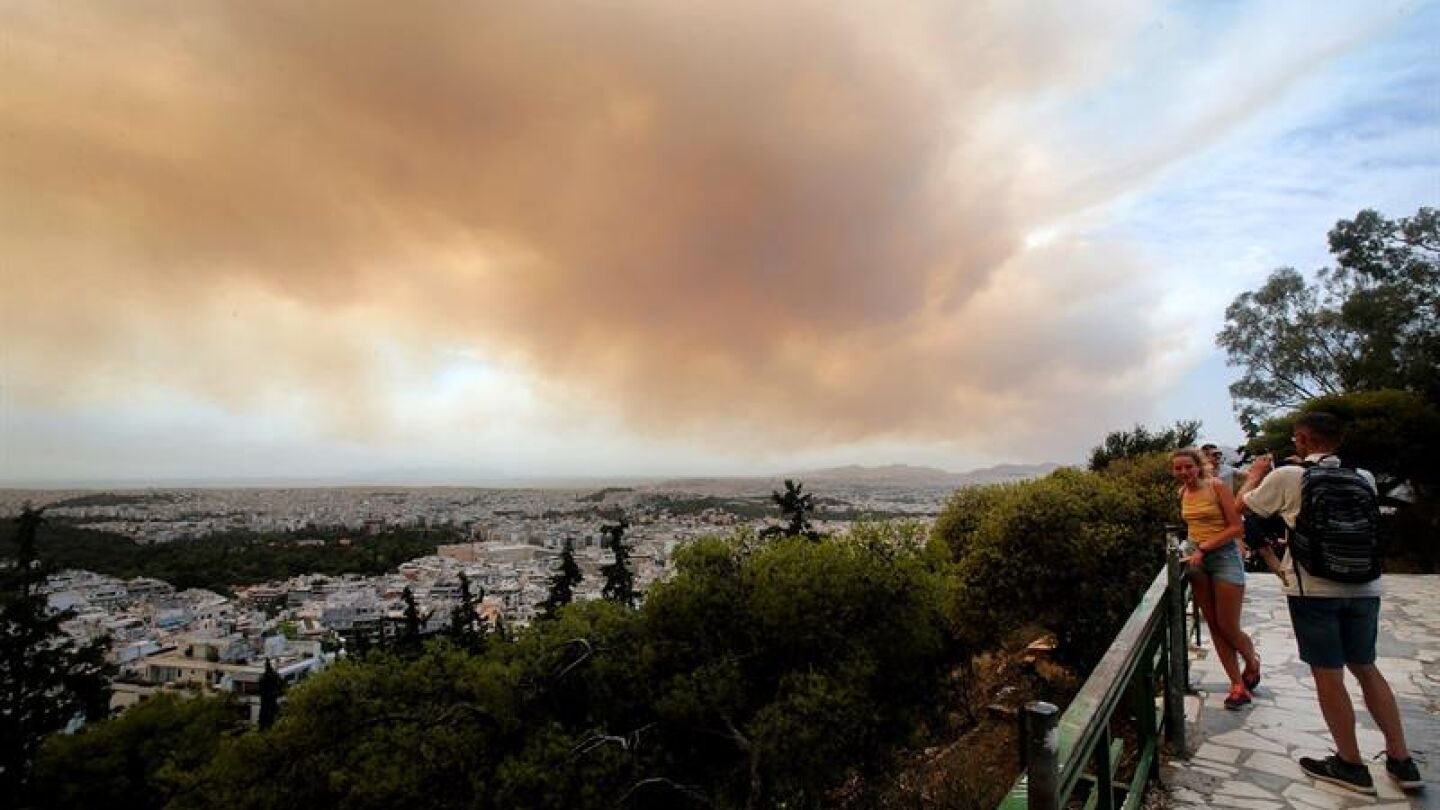 Unos turistas fotograf&iacute;an las nubes densas de humo que se expanden en el cielo debido un incendio en las monta&ntilde;as de Gerania, a 54 km de Atenas