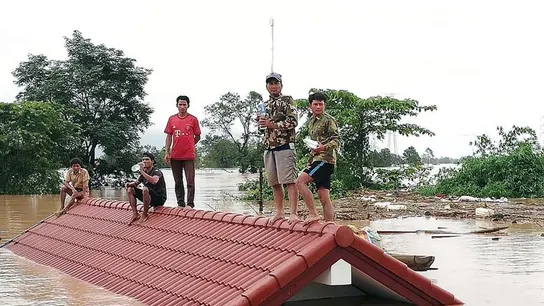 Un grupo de personas aguarda en lo alto de un tejado en una zona inundada tras el derrumbe de una presa Un grupo de personas aguarda en lo alto de un tejado en una zona inundada tras el derrumbe de una presa