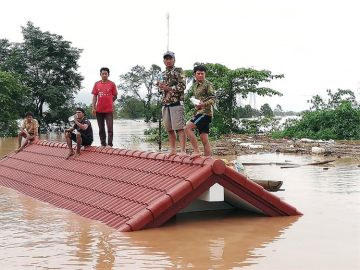 Un grupo de personas aguarda en lo alto de un tejado en una zona inundada tras el derrumbe de una presa Un grupo de personas aguarda en lo alto de un tejado en una zona inundada tras el derrumbe de una presa