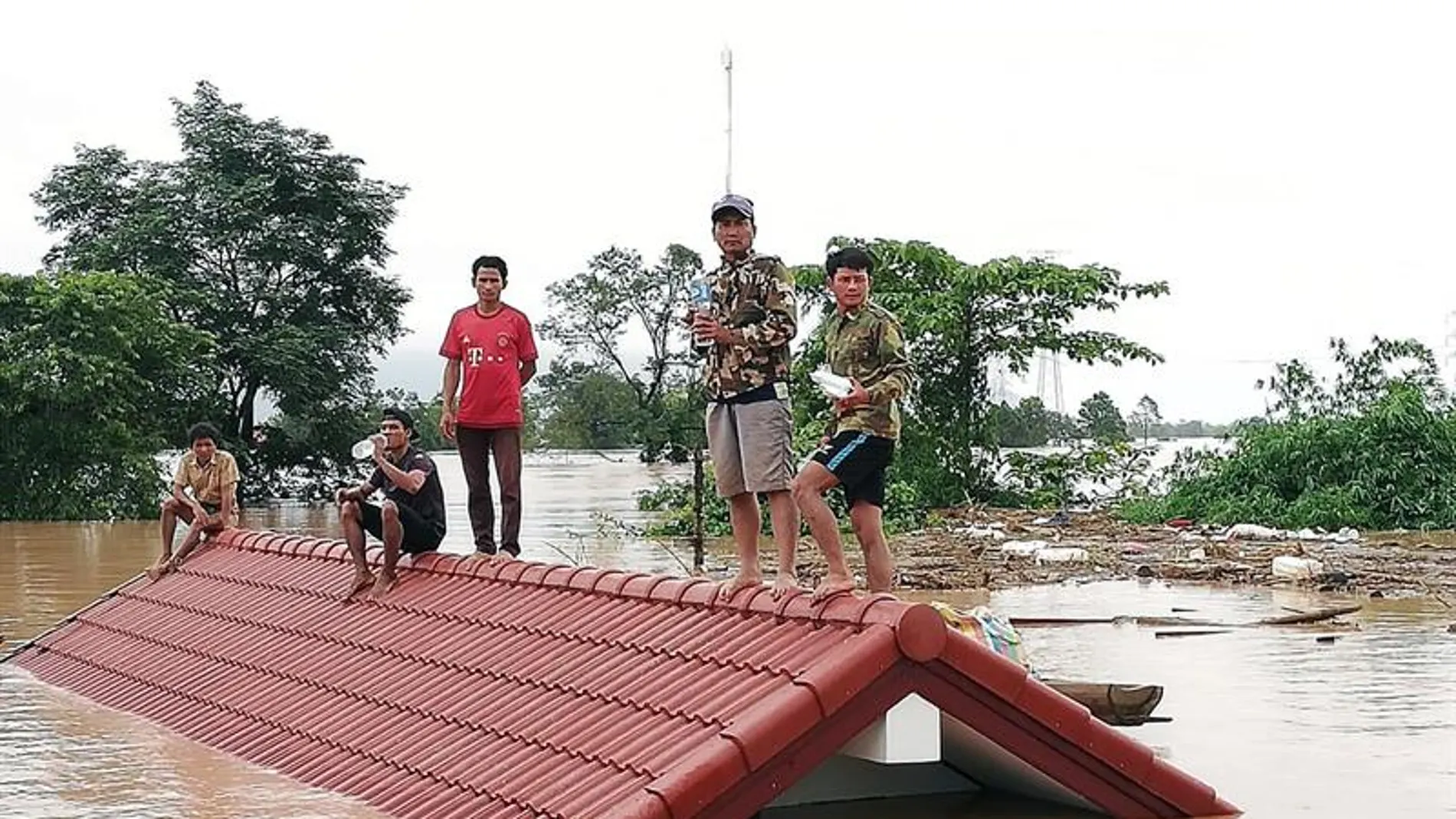 Un grupo de personas aguarda en lo alto de un tejado en una zona inundada tras el derrumbe de una presa 