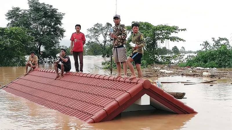 Un grupo de personas aguarda en lo alto de un tejado en una zona inundada tras el derrumbe de una presa 