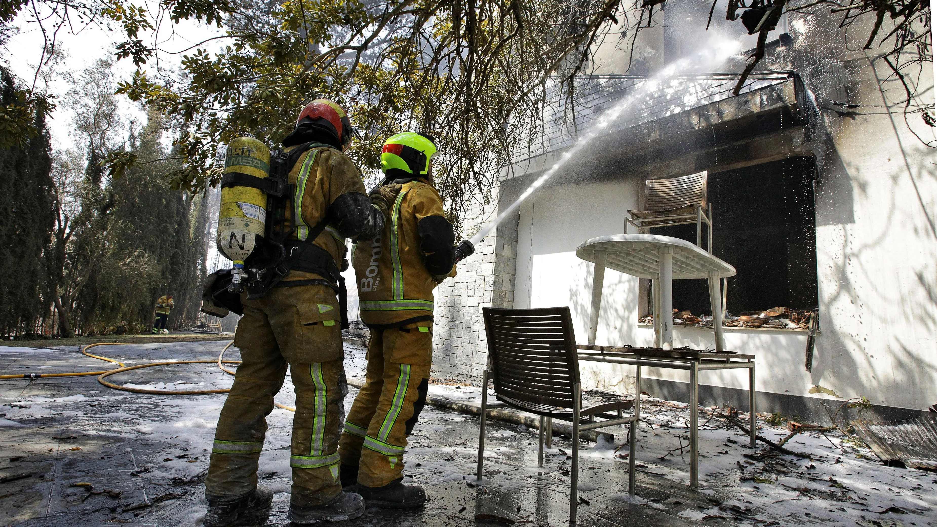 Dos bomberos refrescan el interior de una de las viviendas afectadas por el incendio forestal de Llutxent