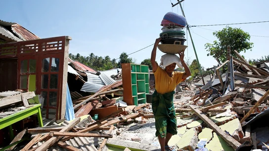 Una mujer carga con sus pertenencias entre los escombros en Lombok Una mujer carga con sus pertenencias entre los escombros en Lombok