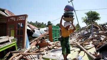 Una mujer carga con sus pertenencias entre los escombros en Lombok