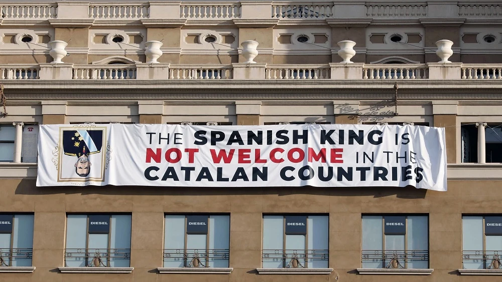 pancarta en contra del rey en la fachada de un edificio de la plaza de Cataluña de Barcelona, donde se va a celebrar el acto central en recuerdo de las víctimas de los atentados del 17A