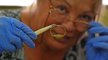 Una arqueóloga limpia un pendiente de oro