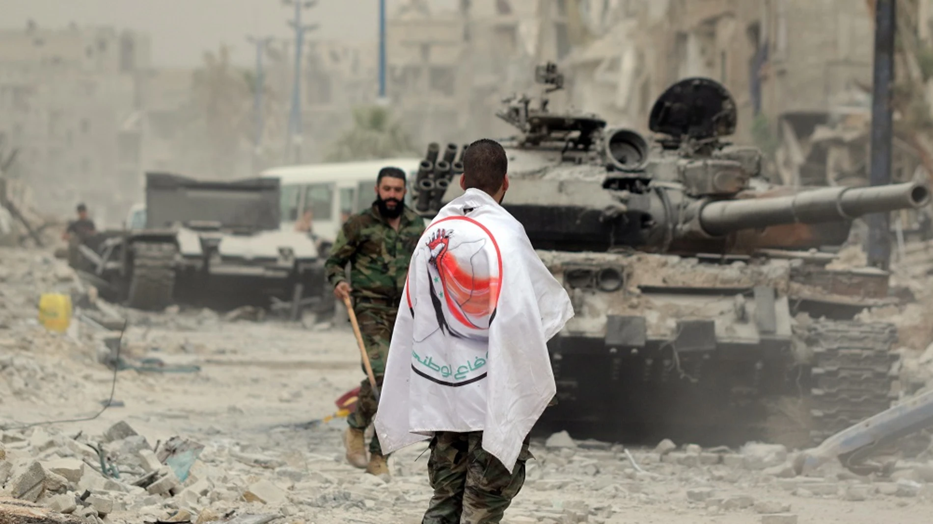 Un soldado del Ejército sirio porta una bandera de la Fuerza de la Defensa Nacional Siria (FDN) en el campamento de Yarmouk, al sur de Damasco