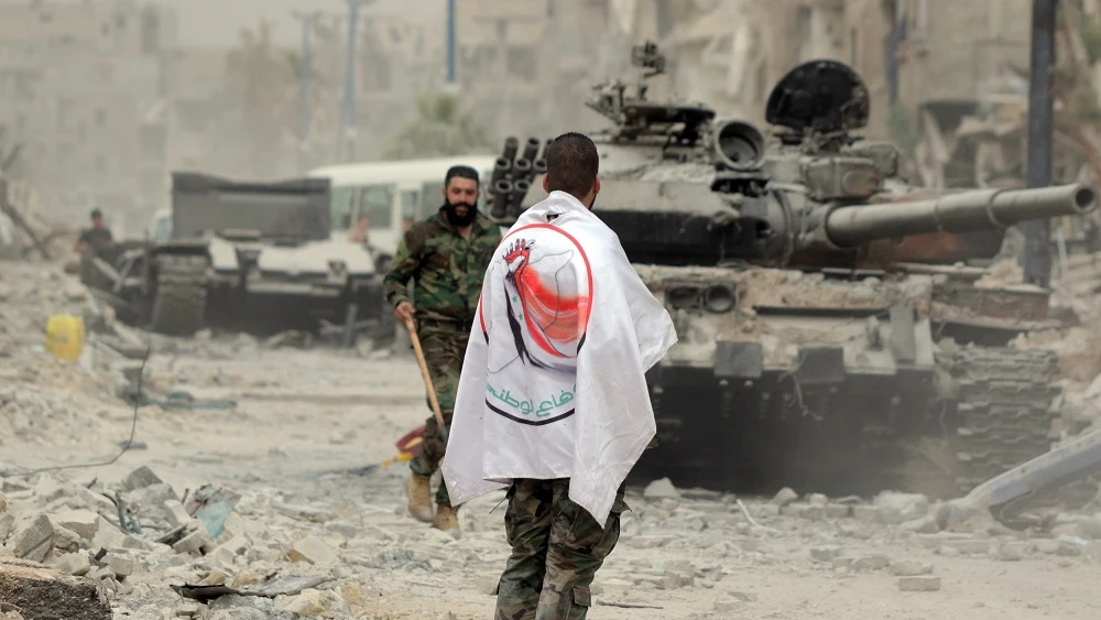 Un soldado del Ejército sirio porta una bandera de la Fuerza de la Defensa Nacional Siria (FDN) en el campamento de Yarmouk, al sur de Damasco