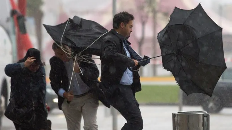 Varias personas sujetan sus paraguas por el fuerte viento