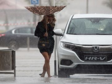 Una mujer sujeta el paraguas intentando que no se le vuele debido al viento Una mujer sujeta el paraguas intentando que no se le vuele debido al viento