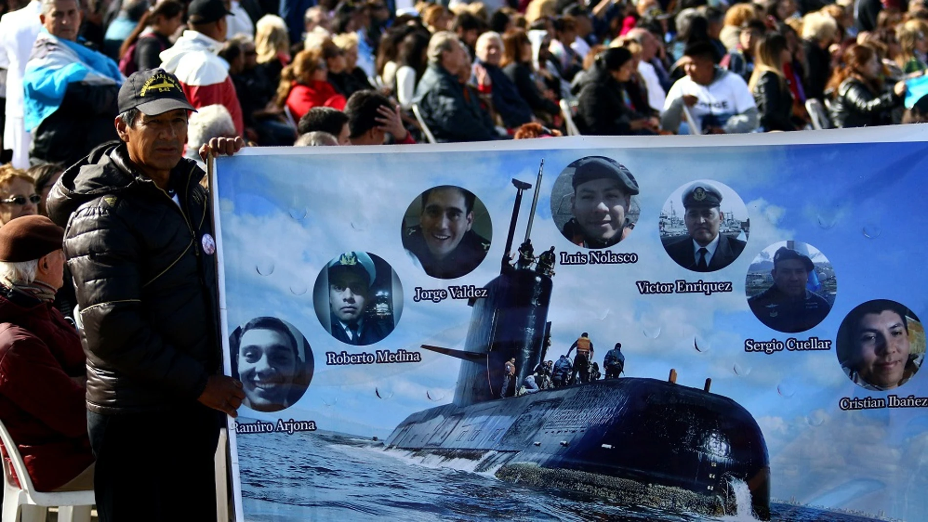Imagen de un hombre que sostiene una pancarta con imágenes de algunos tripulantes del submarino argentino ARA San Juan