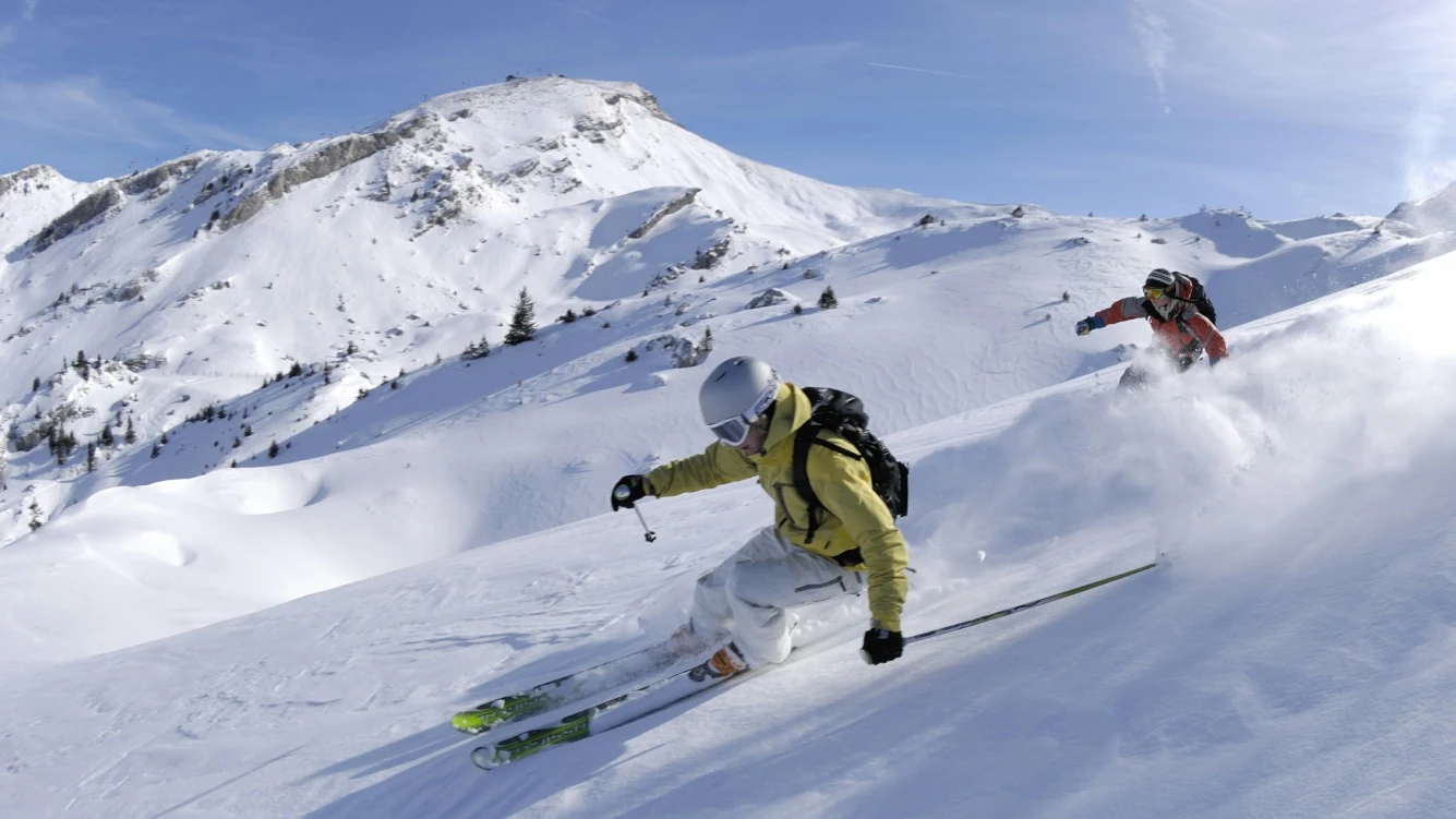 Dos hombres practican esquí. Seis cosas imprescindibles en tu maleta si vas a la nieve