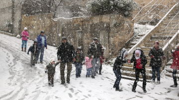 Adultos y niños caminan bajo una intensa nevada caída sobre Damasco.