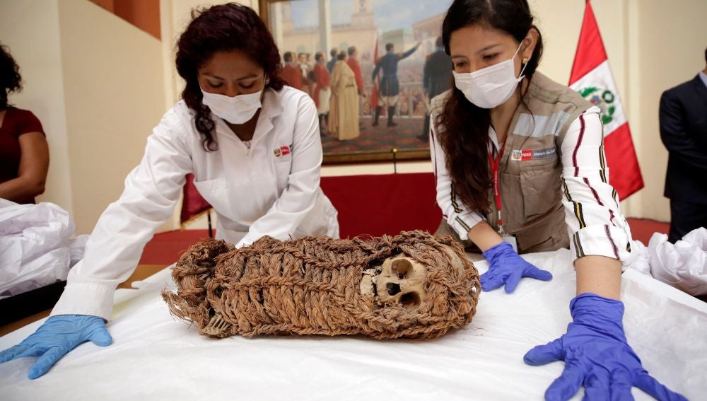 Dos mujeres junto a una momia de un niño de origen aimara
