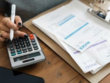 Una mujer revisa sus facturas con la ayuda de una calculadora Una mujer revisa sus facturas con la ayuda de una calculadora