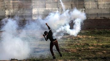 Un palestino devuelve una granada de gas lacrimógeno durante protestas en la frontera entre Israel y Palestina