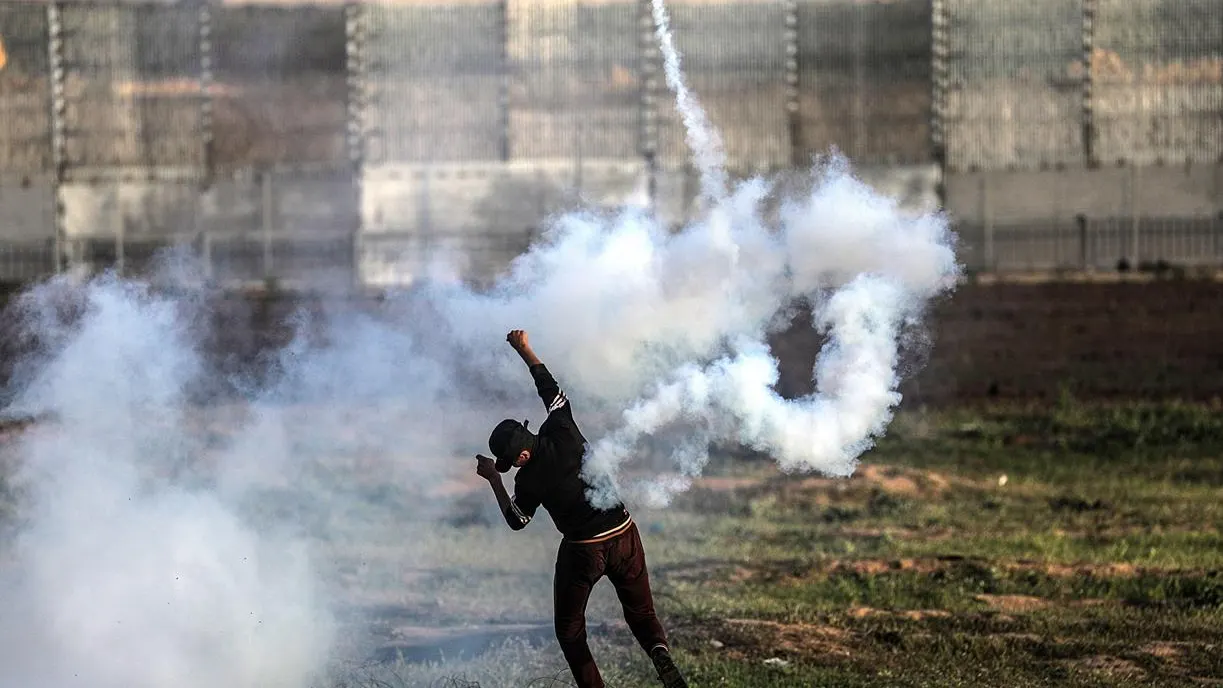 Un palestino devuelve una granada de gas lacrimógeno durante protestas en la frontera entre Israel y Palestina