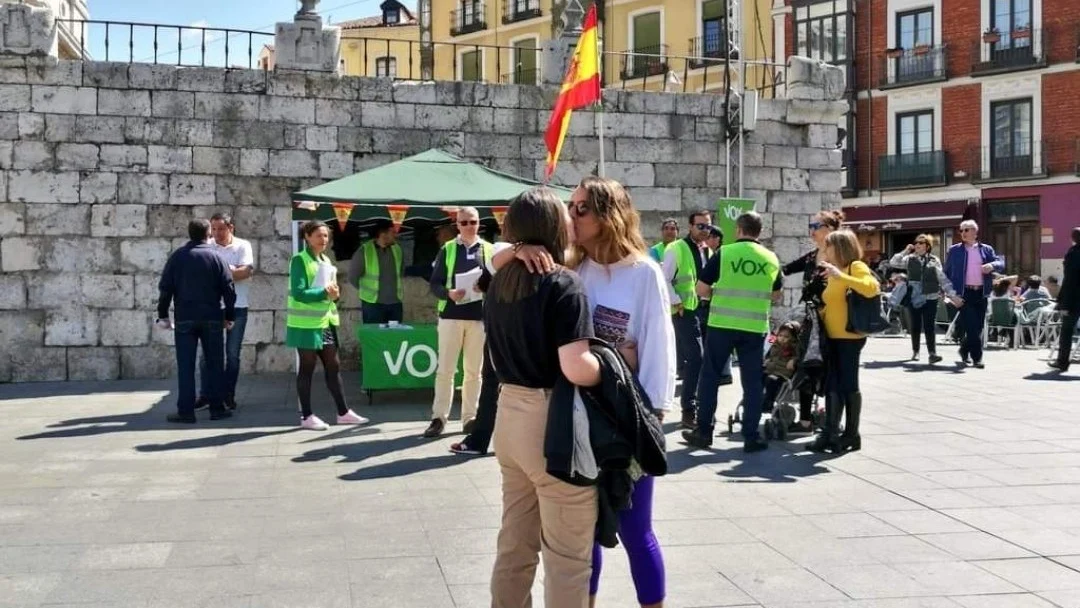 Una pareja de lesbianas se besa frente a un puesto de Vox